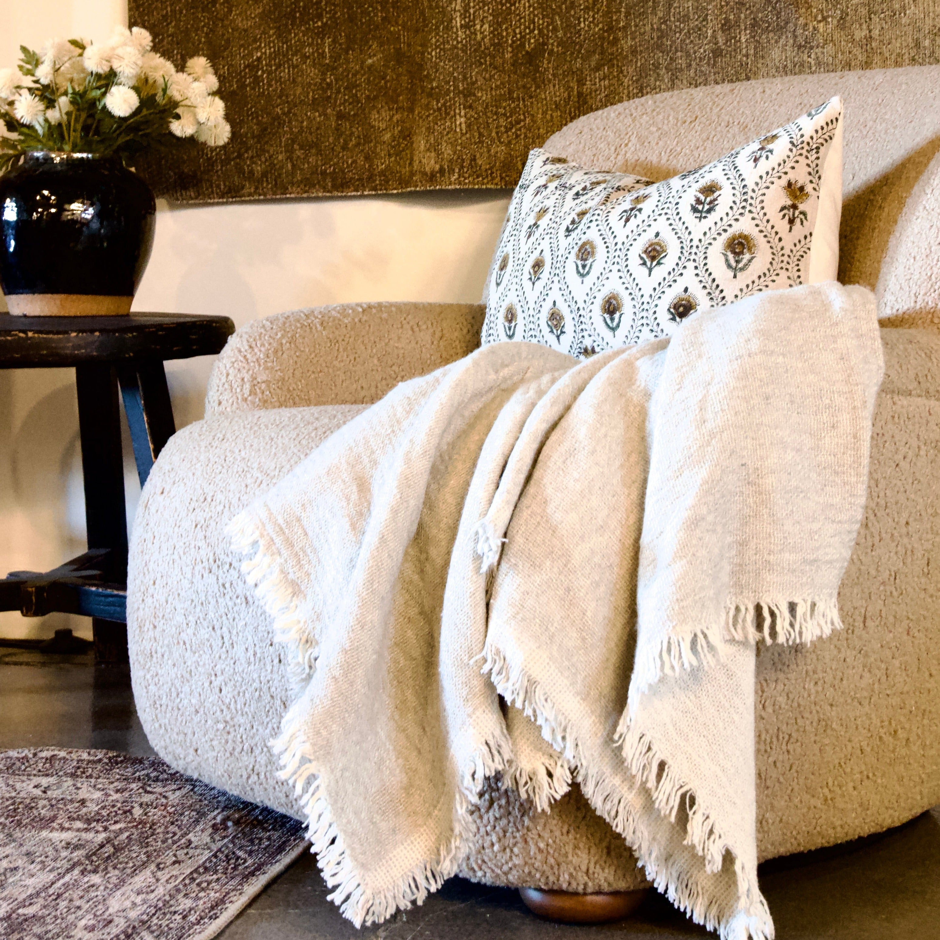 Floral block print pillow with green vines on beige linen styled on couch with ivory throw.