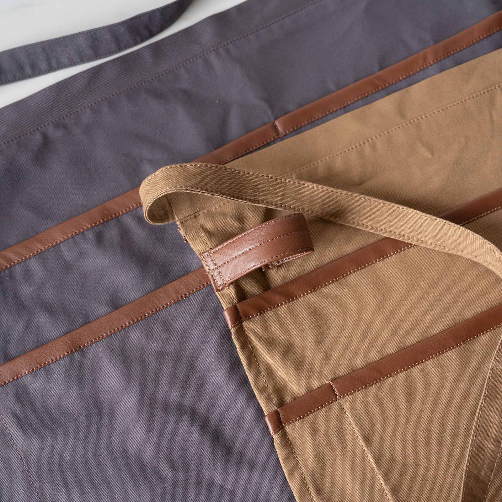 Utility aprons in grey and tan with vegan leather trim